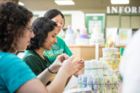 Three people use rubber bands to bind items together for a display for University Life's Summer Day of Service.